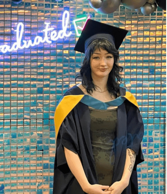 Woman with shoulder length black hair smiling wearing black, yellow and blue graduation gown.