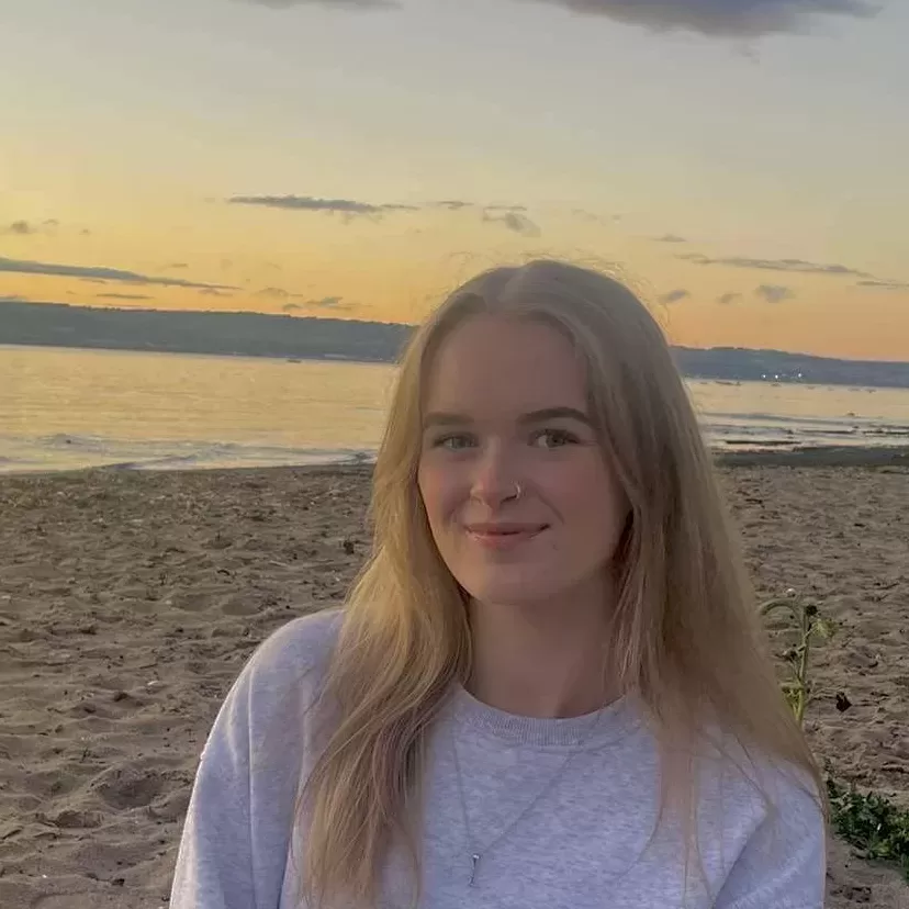 Woman with long blonde hair wearing grey sweatshirt sitting on a beach